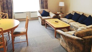 A hotel room with a dining table, two armchairs, a sofa, and a small side table with a lamp.