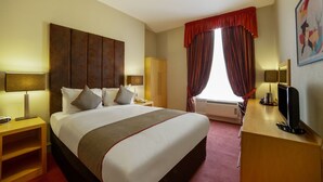 A hotel room with a large bed, a desk with a computer, a wardrobe, and a window with curtains.