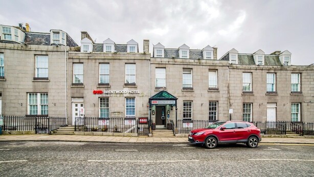 A multi-story hotel with a traditional facade, a red car parked in front, and a clear sky.