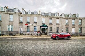 Ein mehrstöckiges Hotel mit traditioneller Fassade, ein rotes Auto davor und ein klarer Himmel.