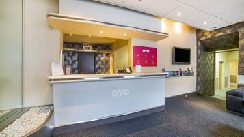 A reception desk with a digital clock, a sign for OYO, and a flat-screen TV mounted on the wall.
