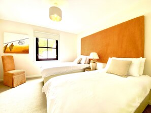 Une chambre d’hôtel avec un grand lit, un plus petit lit, une chaise, une table de chevet, une lampe, une fenêtre et un tableau au mur.