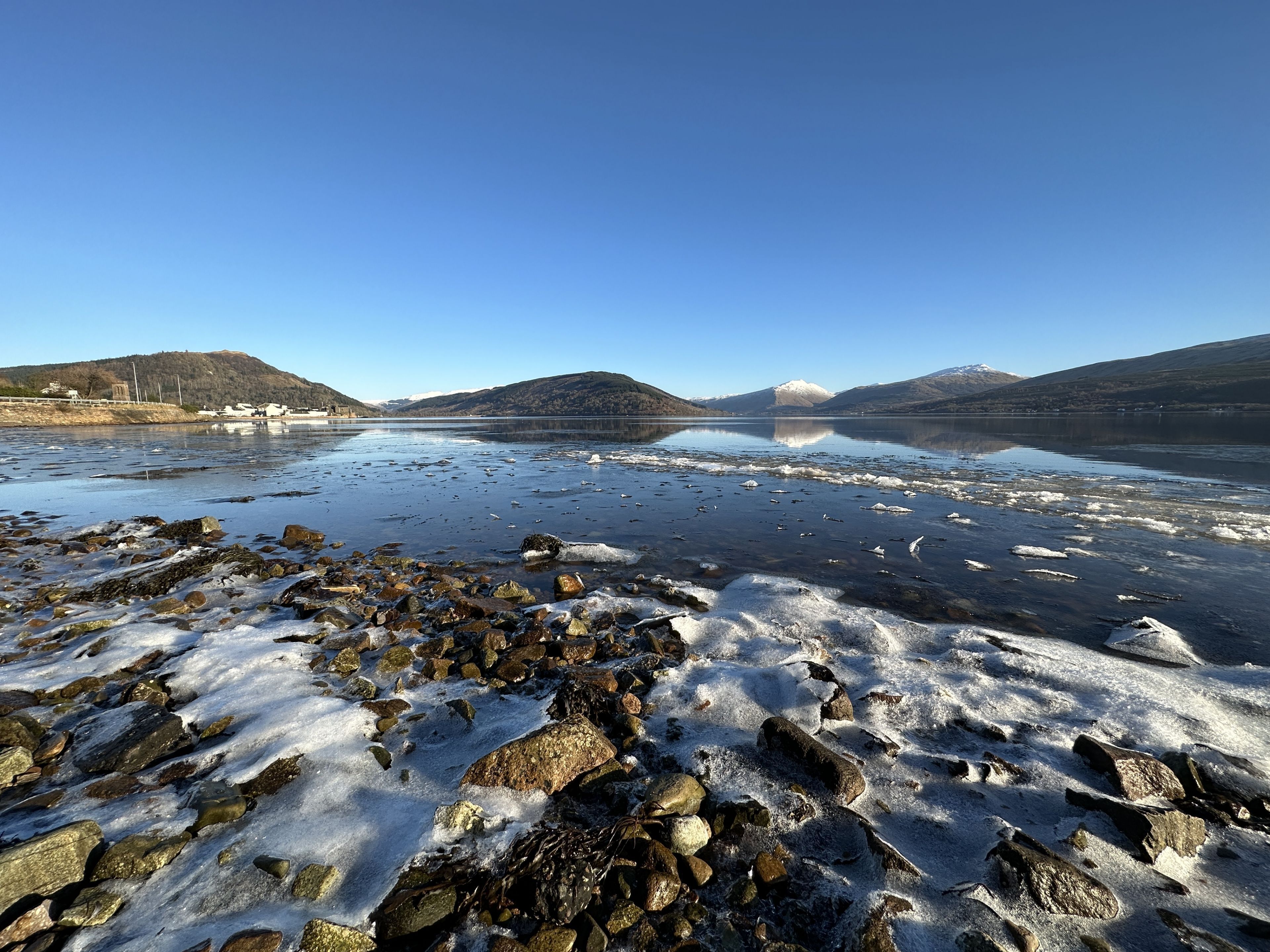 A rocky shoreline with a clear lake and distant mountains.