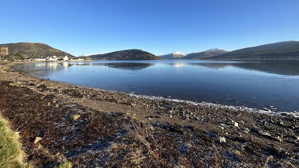 Un llac tranquil amb muntanyes al fons i una riba rocosa.