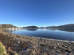 Un lago tranquilo con montañas al fondo y una costa rocosa.