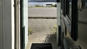 Una porta que dona a una zona d'aparcament amb una banca i muntanyes al fons.