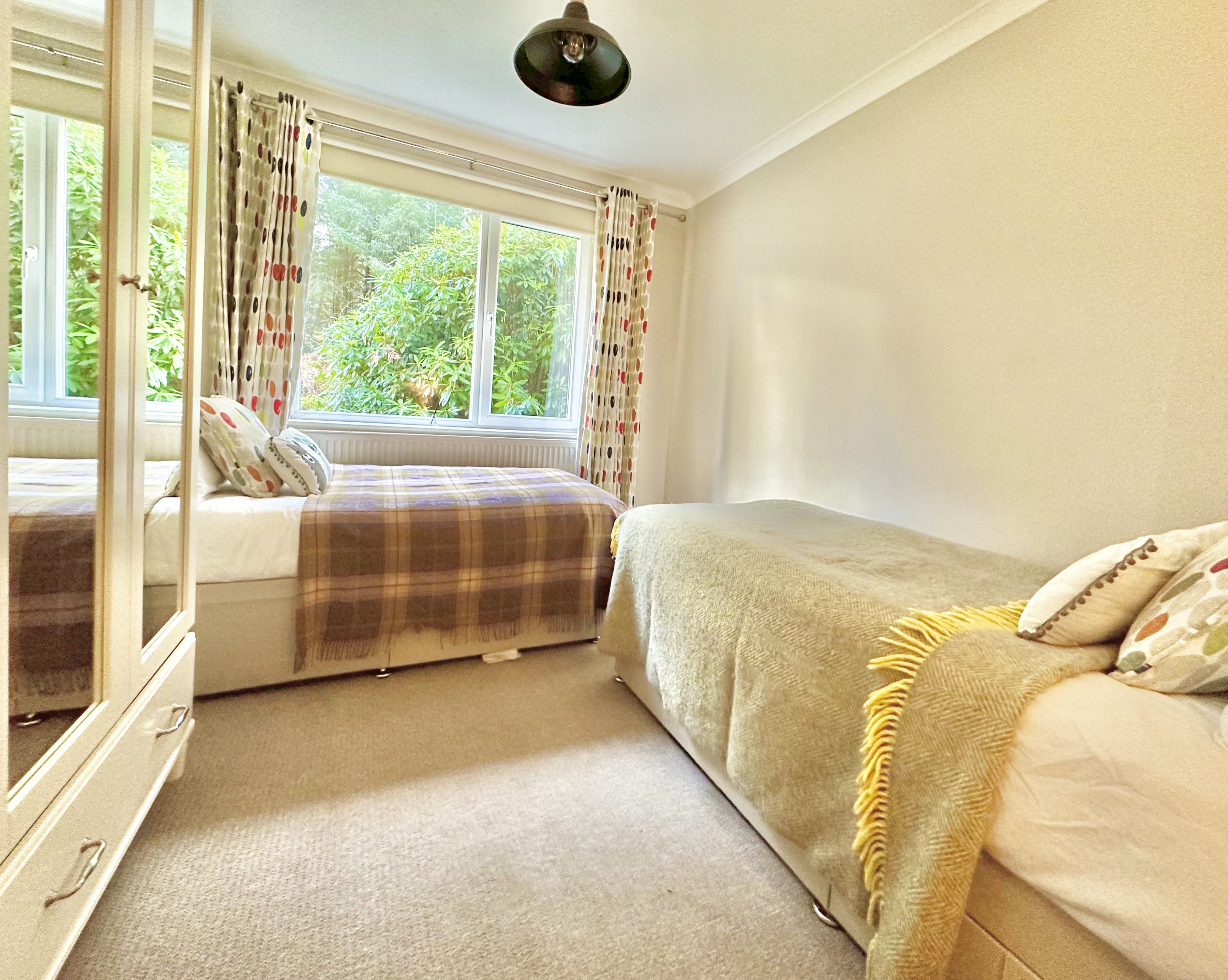 A bedroom with a bed, a dresser, a mirror, and a window with curtains.