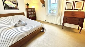Ein Schlafzimmer mit Bett, einem Holzschrank, einem Bücherregal, einem Fenster mit Vorhängen, einem Heizkörper und einem gerahmten Bild an der Wand.