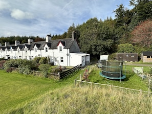 Une rangée de maisons blanches aux toits noirs, un champ d’herbe et un trampoline entouré d’une clôture.