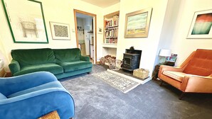 Ein Wohnzimmer mit einem grünen Sofa, einem blauen Sofa und einem orangefarbenen Sessel, einem Kamin und einem Bücherregal.
