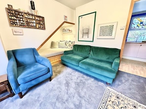 Un salon avec un fauteuil bleu, un canapé turquoise et un escalier menant à un lit en mezzanine.