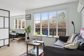 Una sala de estar moderna con un sofá, una mesita de centro, una estantería y un ventanal con vistas a árboles.