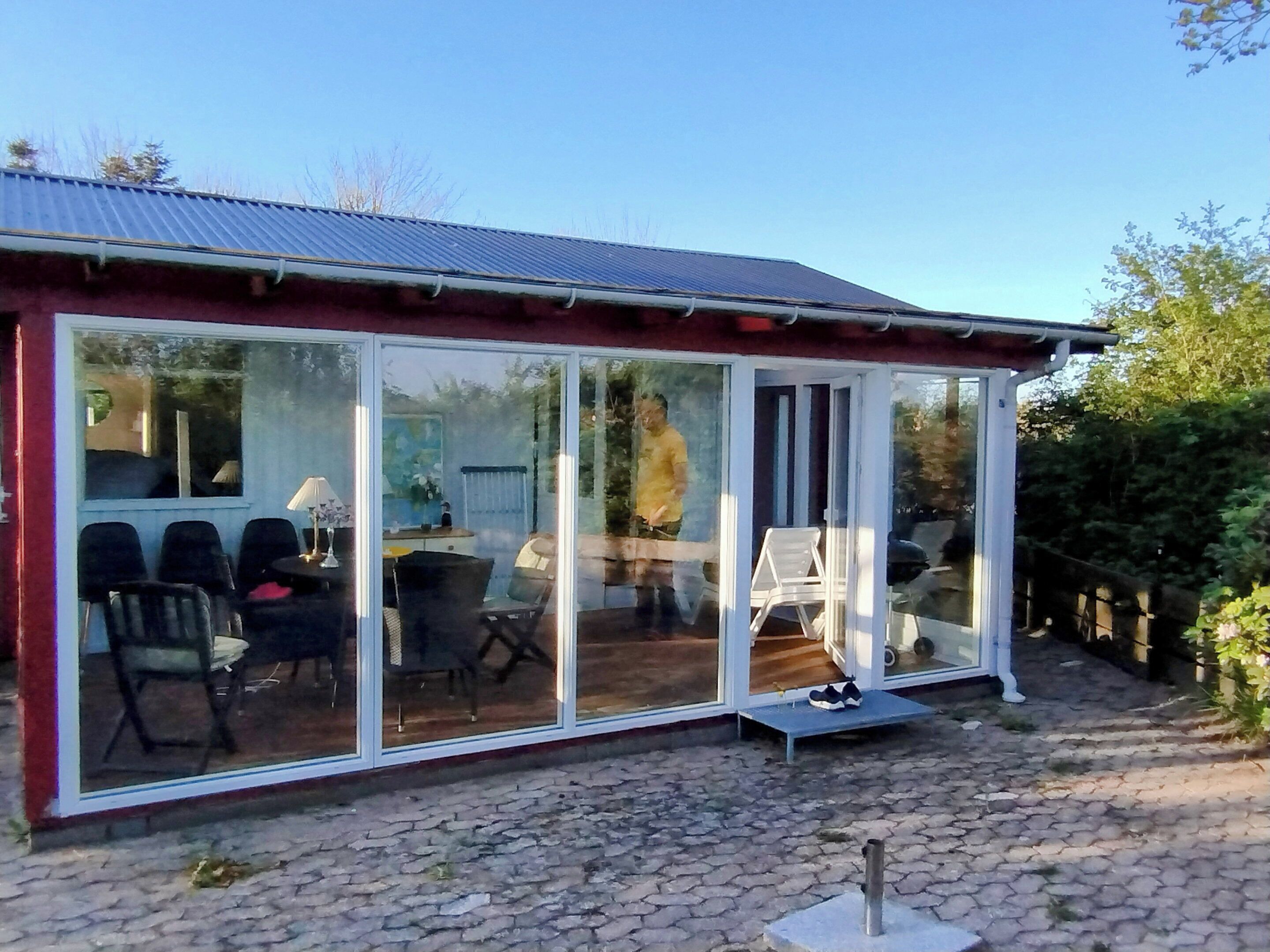 Una habitación con paredes de vidrio que incluye una mesa, sillas, un banco y un pequeño escalón hacia la puerta.