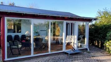 Una habitación con paredes de vidrio que incluye una mesa, sillas, un banco y un pequeño escalón hacia la puerta.