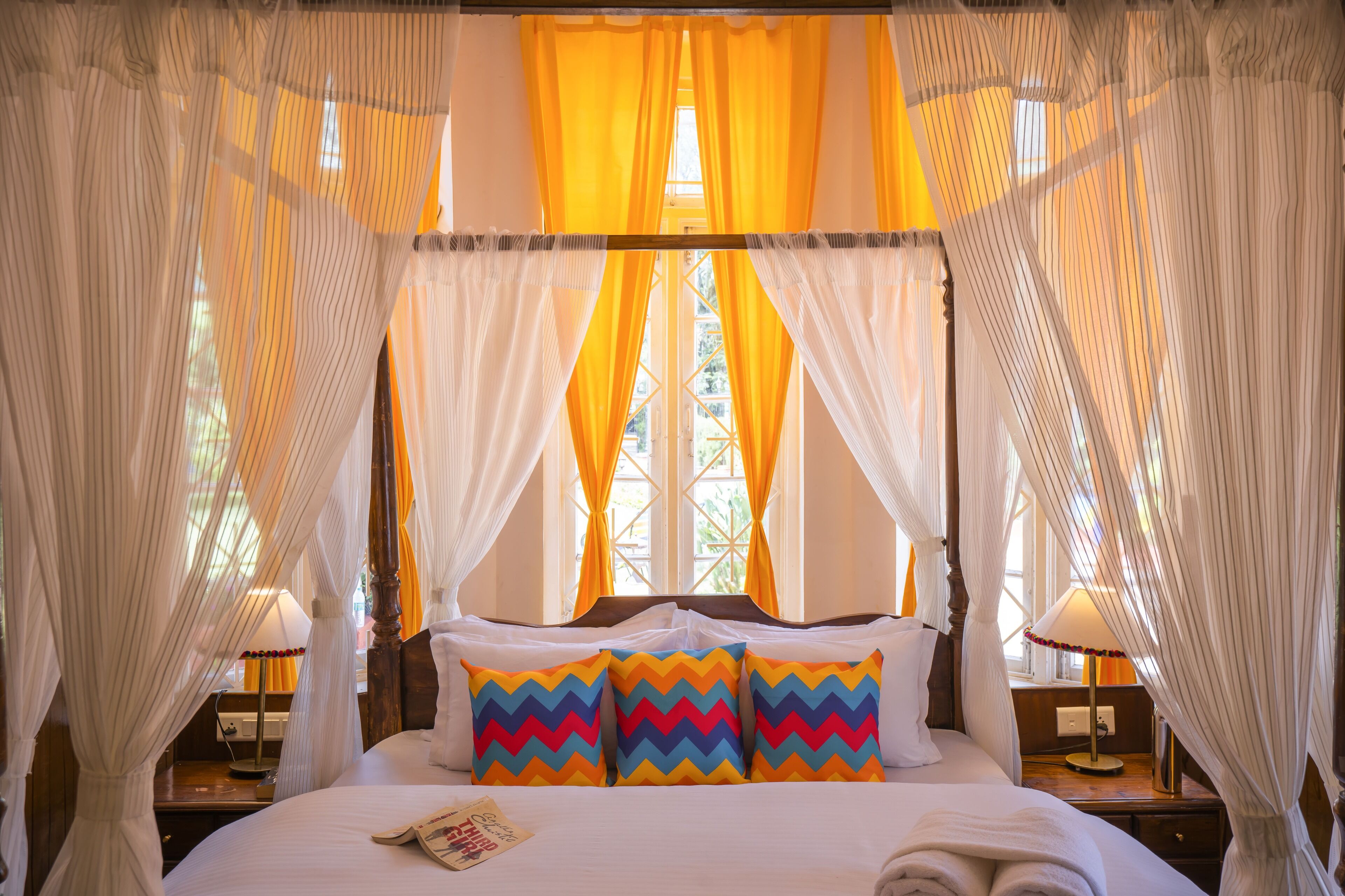 Una cama con dosel y cortinas, una mesita de noche con lámpara y una ventana con cortinas.