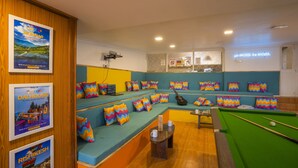 A pool table in a room with a green pool table, a pool cue, and a billiards ball. There are colorful zigzag pillows on the seating area. - goSTOPS Ooty (Ooty)