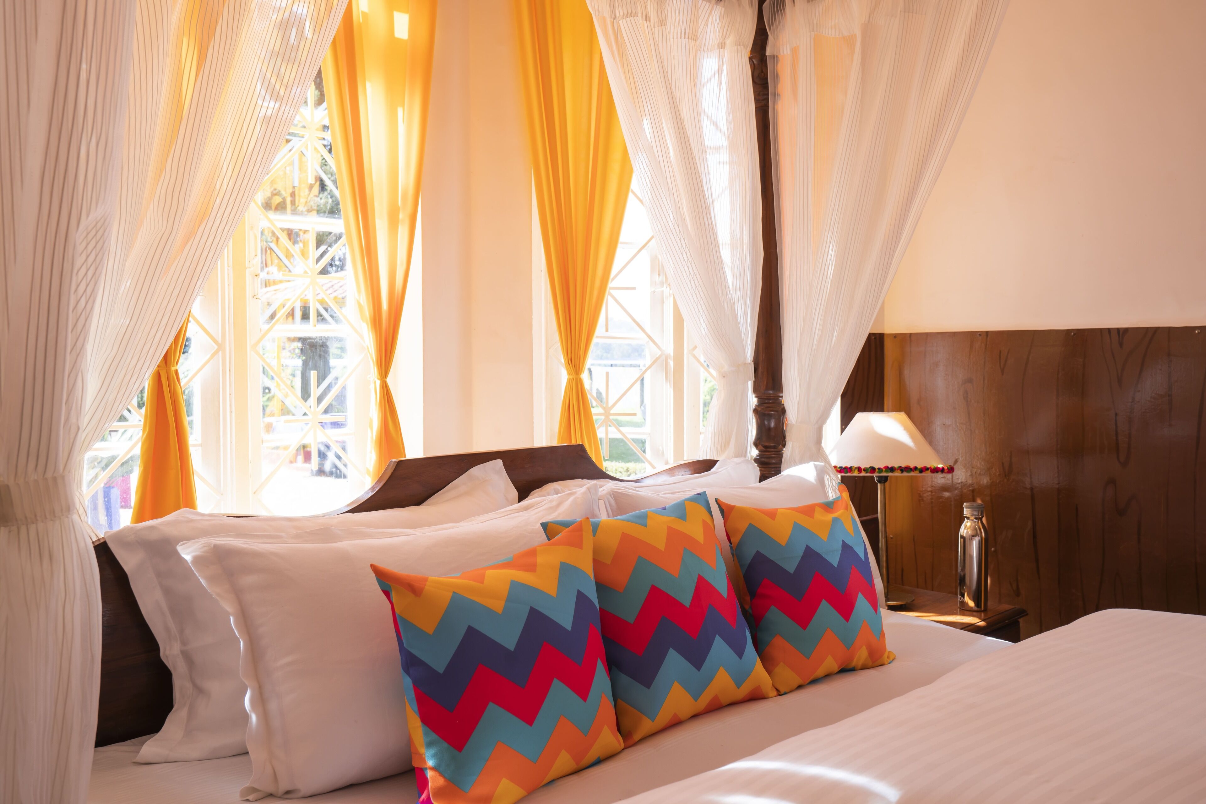 Una cama con sábanas blancas, almohadas de colores en zigzag y un cabecero de madera.