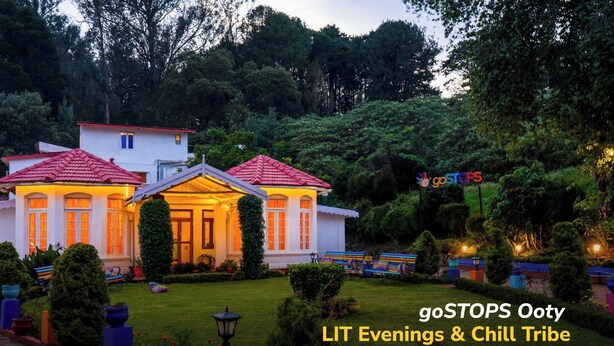 A well-lit house with a red roof, surrounded by lush greenery and a garden with colorful benches. - goSTOPS Ooty (Ooty)