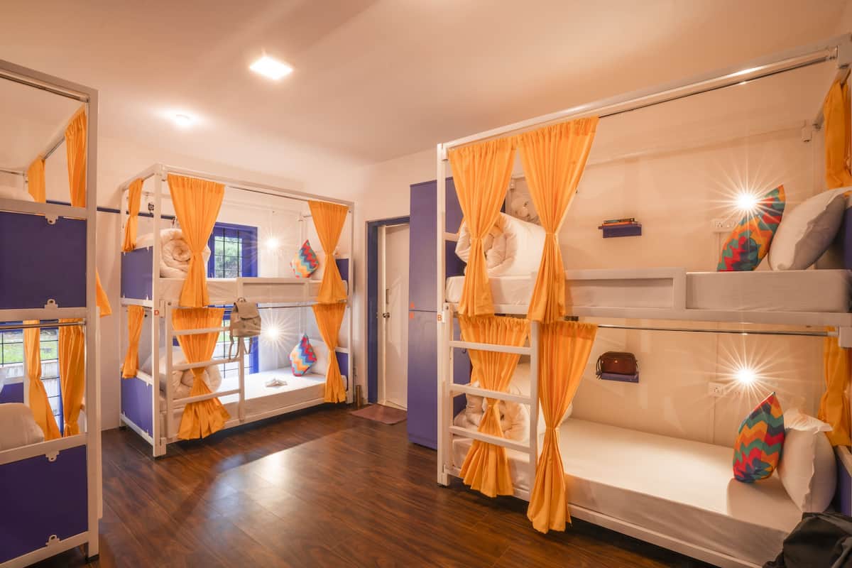 A room with bunk beds, orange curtains, and a small window with a view.