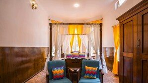 A room with a wooden floor, a bed with a canopy, two armchairs with colorful cushions, and a wooden wardrobe. - goSTOPS Ooty (Ooty)