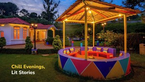 A gazebo with colorful seating and a well-lit outdoor area, surrounded by a house with a red roof. - goSTOPS Ooty (Ooty)