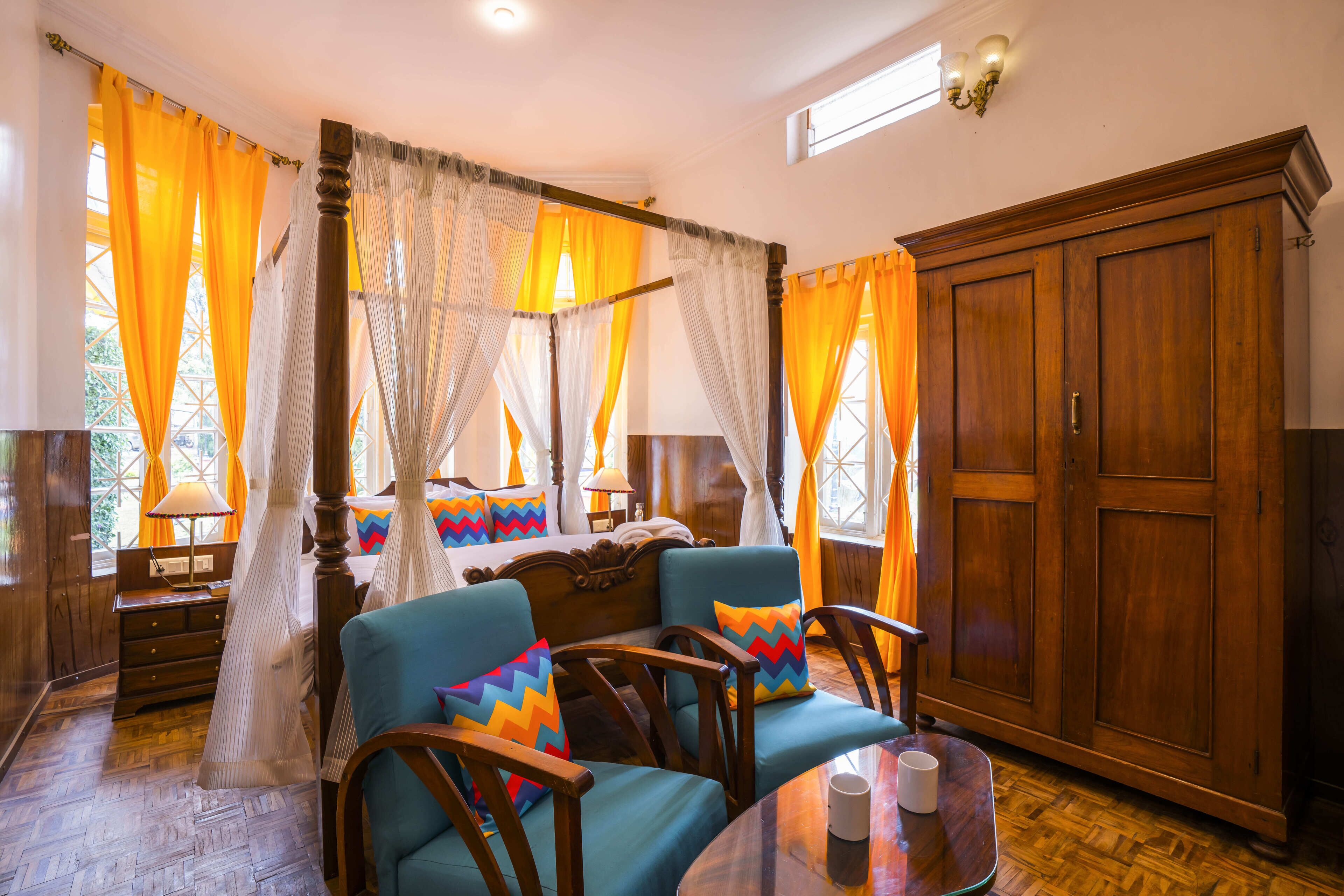 A room with a four-poster bed, a wooden wardrobe, and a dining table with chairs.