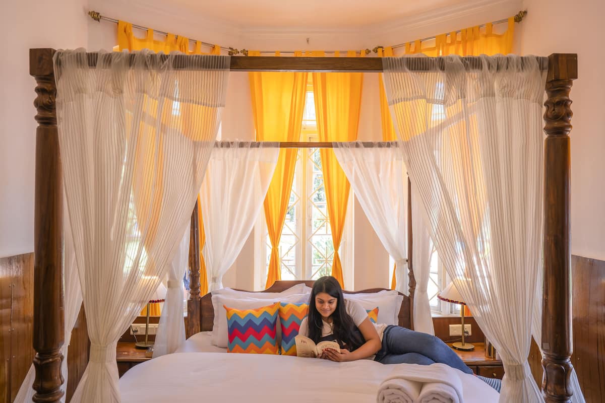 A room with a four-poster bed, a bedside table, and a window with curtains.