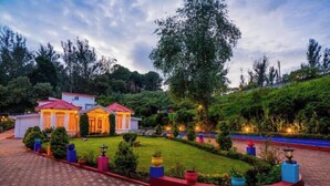 A hotel with a red-roofed main building, surrounded by well-maintained gardens and a paved driveway. - goSTOPS Ooty (Ooty)