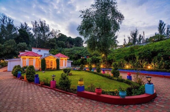 A hotel with a red-roofed main building, surrounded by well-maintained gardens and a paved driveway. - goSTOPS Ooty (Ooty)