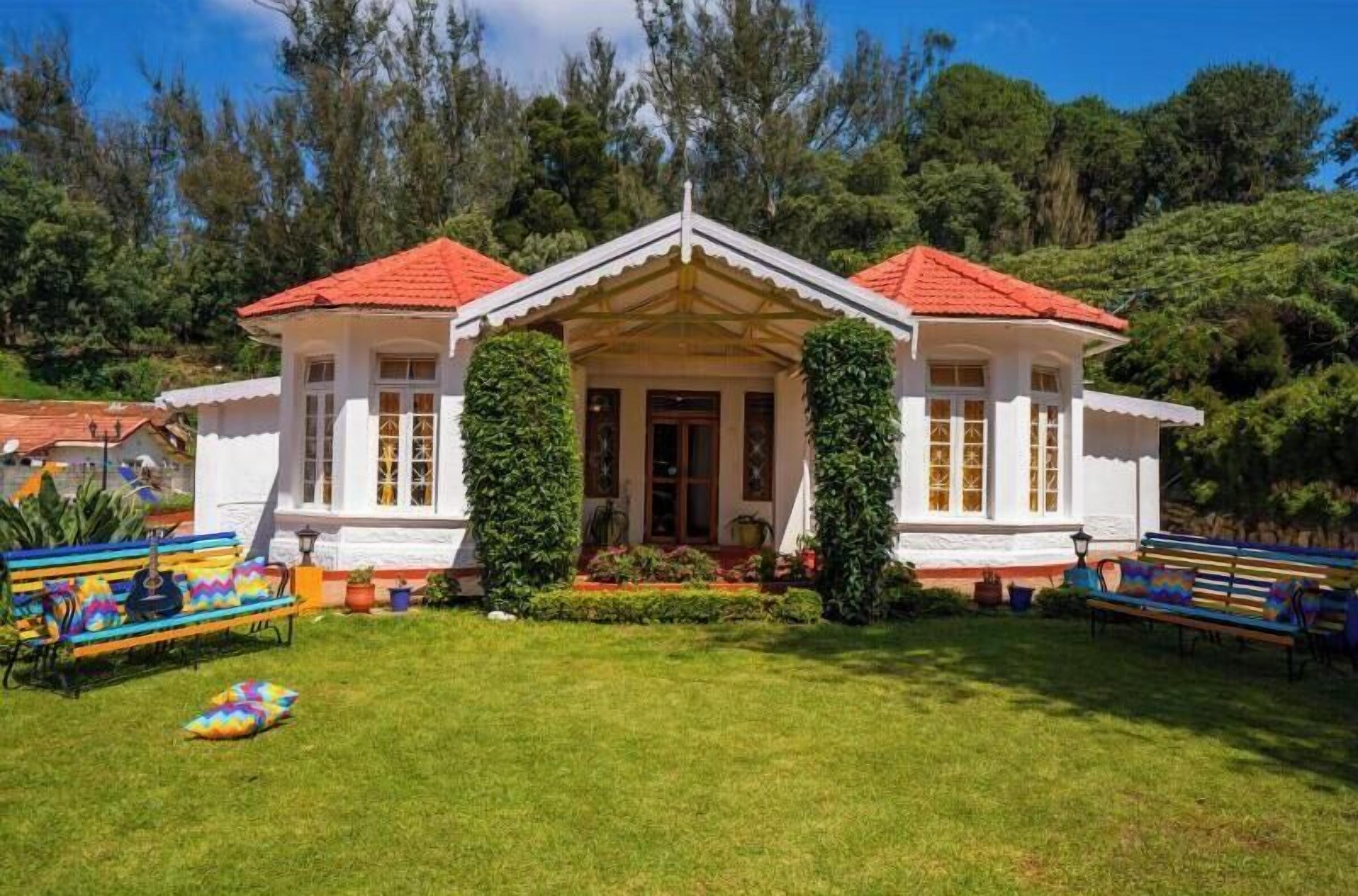 A white building with a red roof, surrounded by greenery and benches.