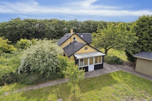 Een geel huis met een schuin dak, omringd door groen en bomen.