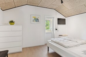 Een slaapkamer met een bed, een witte dressoir, een kleine plant, een ingelijste foto en een televisie.