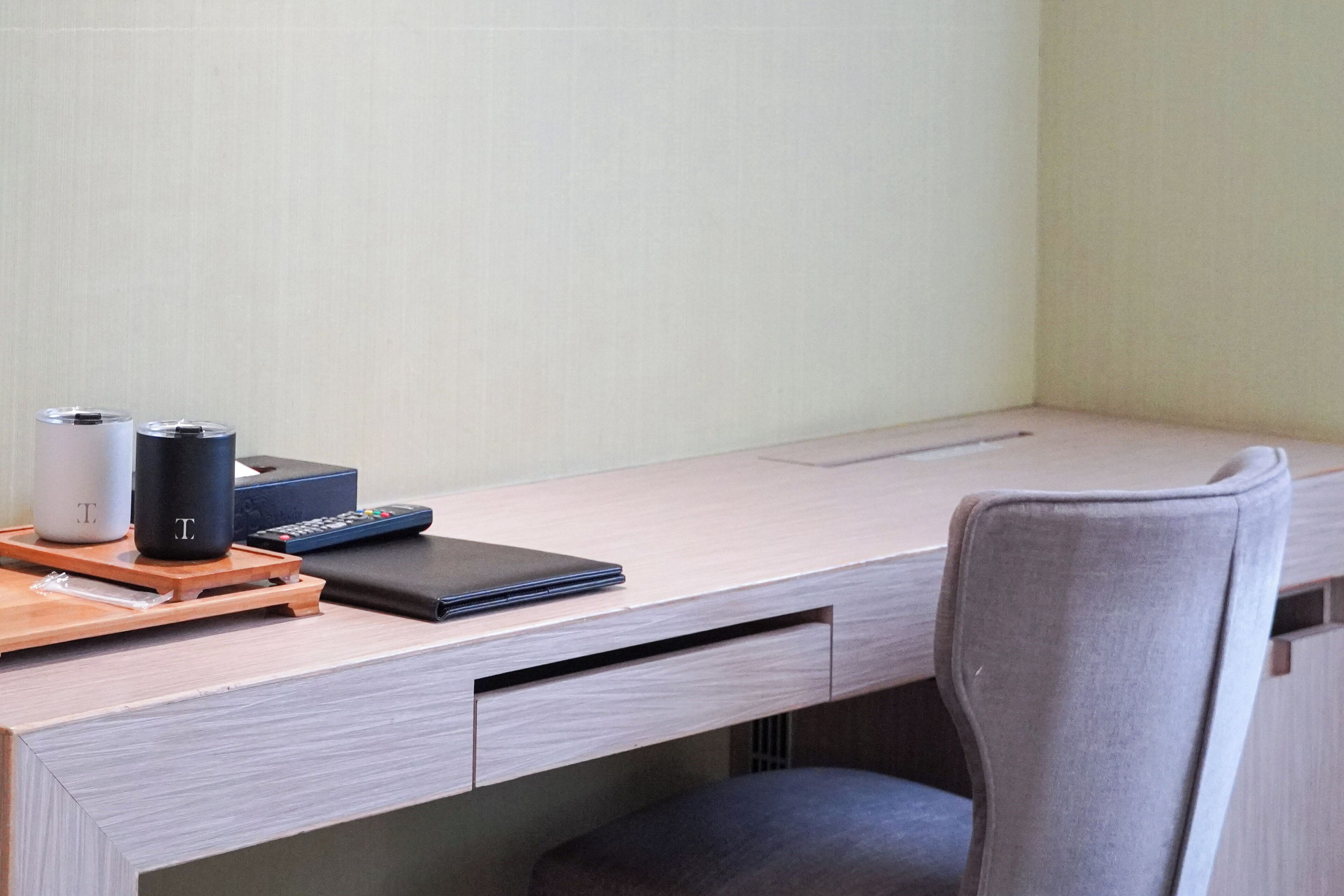 A desk with a laptop, a remote control, and two containers.