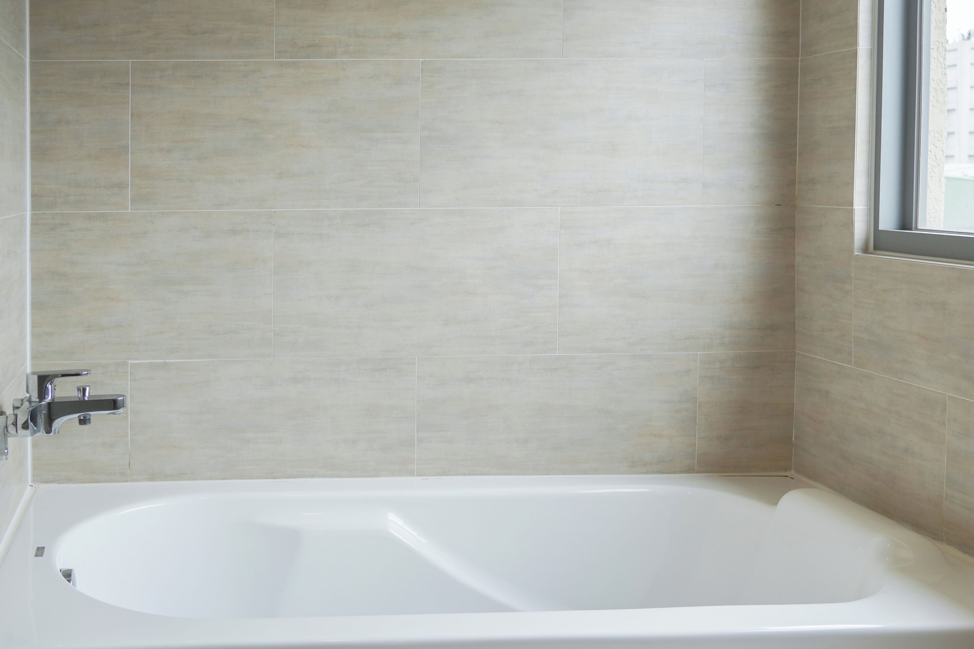 A modern bathroom with a large bathtub, tiled walls, and a window.