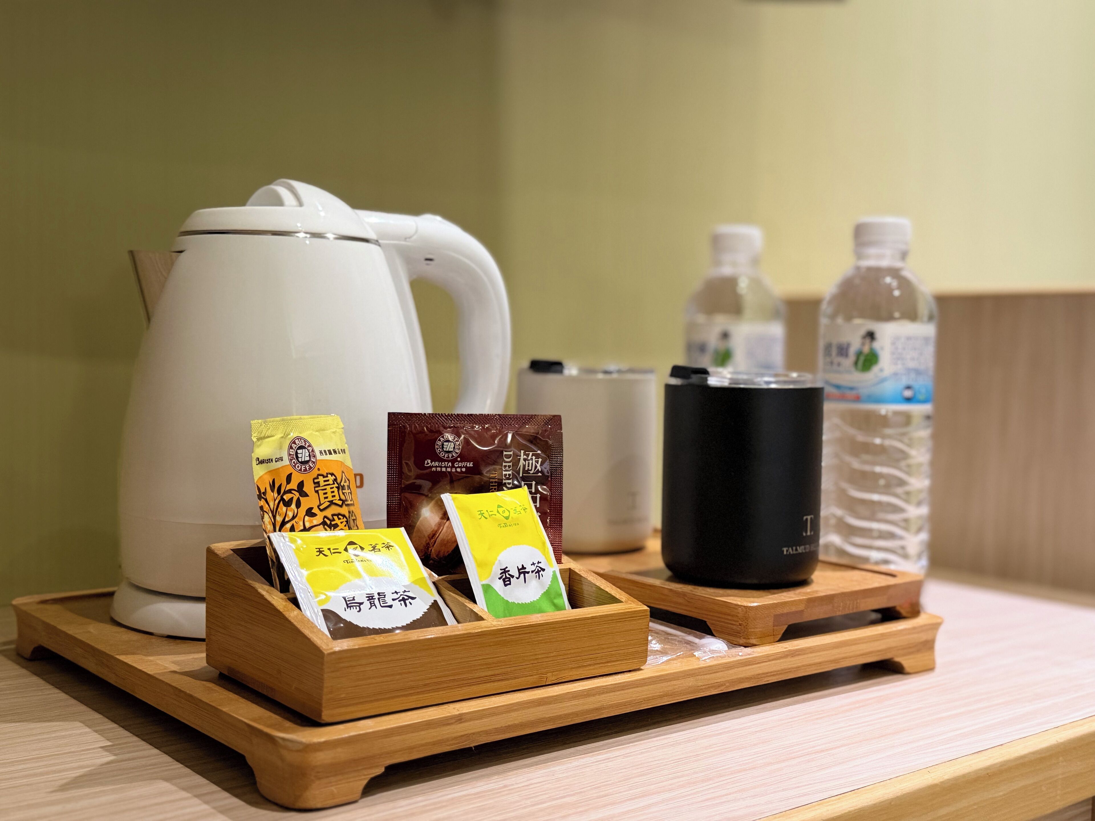 Una bandeja de madera con sobres de té, una taza negra y una botella de agua sobre una mesa.