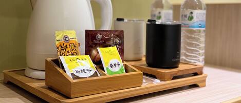 Una bandeja de madera con sobres de té, una taza negra y una botella de agua sobre una mesa.