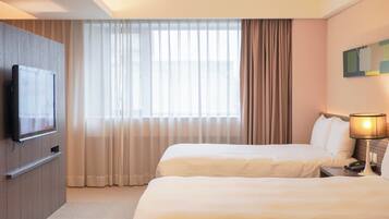 Une chambre d’hôtel avec deux lits, un téléviseur fixé au mur et une grande fenêtre avec des rideaux.