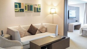 Ein modernes Hotelzimmer mit Sofa, Couchtisch, Lampe und Fernseher.