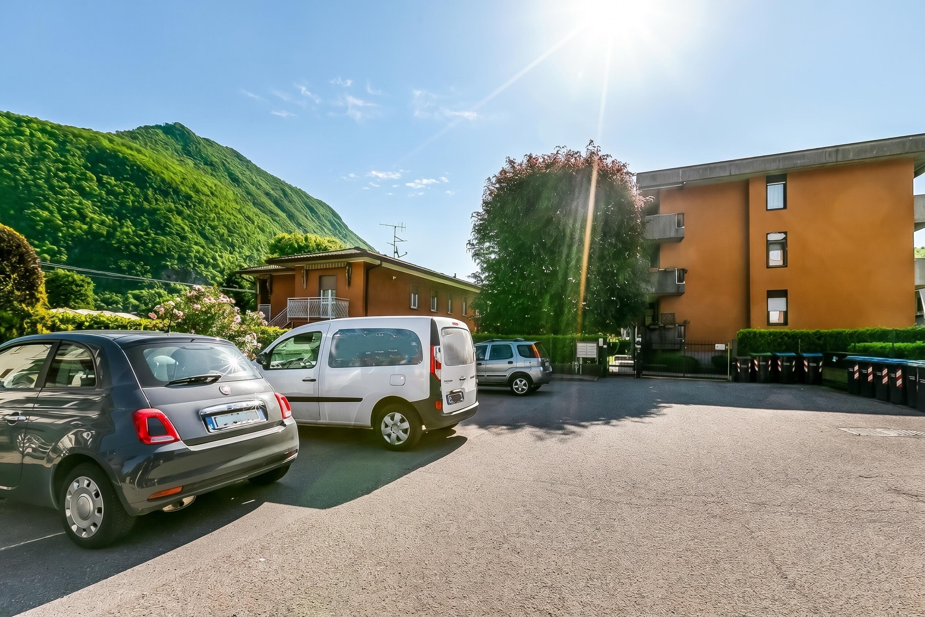 Un aparcamiento con coches, un edificio con varias ventanas y una montaña al fondo.