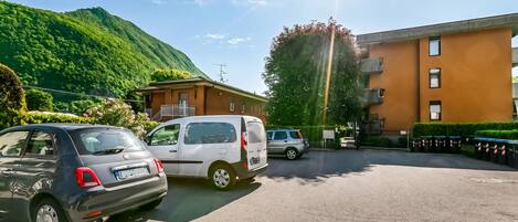 Un aparcamiento con coches, un edificio con varias ventanas y una montaña al fondo.
