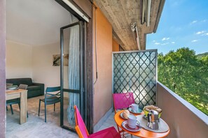 A balcony with a table, chairs, and a view of greenery.