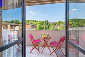 Un balcon avec une table et des chaises, une vue sur les bâtiments et la verdure, et un ciel dégagé.