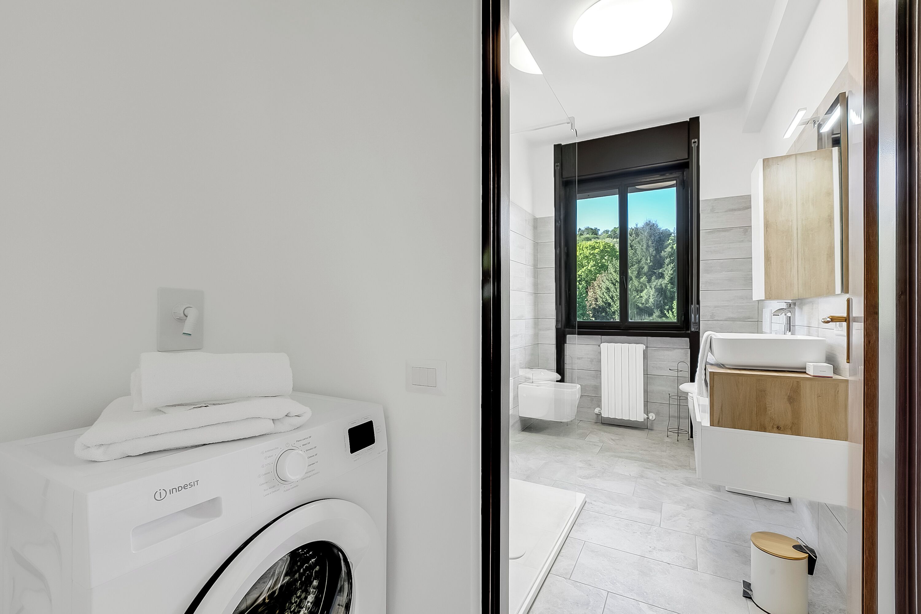 Une salle de bain moderne équipée d’un lave-linge, d’une grande fenêtre et d’un meuble-lavabo en bois.