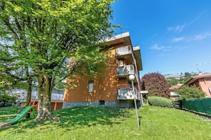 A building with a playground, including a slide, and a large tree in front. - La Dolce Laveno (Laveno Mombello)