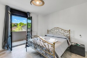 Une chambre à coucher avec un lit, une table de chevet, une vue sur l’extérieur par une porte ouverte et un luminaire au plafond.