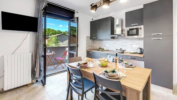 A modern kitchen with a dining table, chairs, and a view through an open door. - La Dolce Laveno, Balcony Apartment With A/C (Laveno Mombello)