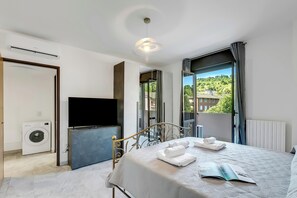 A modern bedroom with a bed, a television, a washing machine, and a view of a green landscape.