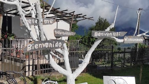 Ein Fahrrad vor einem Wegweiser mit verschiedenen Willkommensschildern in unterschiedlichen Sprachen, einem Metallzaun und einem Gebäude im Hintergrund.