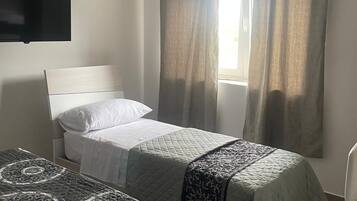 Ein Hotelzimmer mit zwei Einzelbetten, einem an der Wand befestigten Flachbildfernseher und einem Fenster mit Vorhängen.