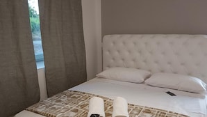 Ein ordentlich bezogenes Bett mit einem gemusterten Überwurf, zwei aufgerollte Handtücher und ein Smartphone auf dem Bett.